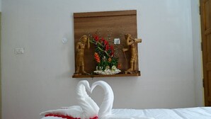 Une chambre d’hôtel avec un lit, une étagère fixée au mur ornée d’objets décoratifs et une serviette en forme de cygne posée sur le lit.