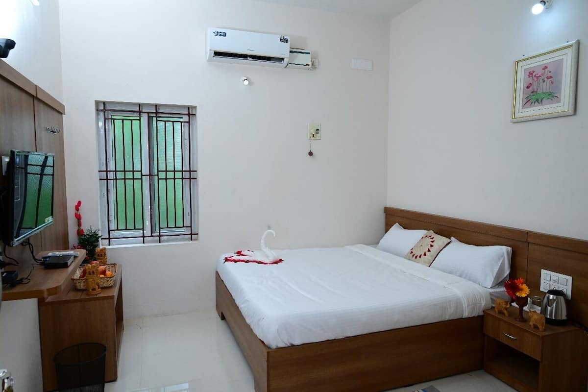 A hotel room with a wooden bed, a desk with a computer, a window with bars, an air conditioner, and a small plant.