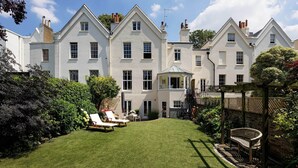 A large, white, multi-story building with a well-maintained lawn and outdoor seating area. - Majestic in Kensington, by Veeve (London)
