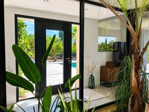 A modern interior with a glass door leading to an outdoor pool area, a wooden cabinet, and a vase with dried plants.