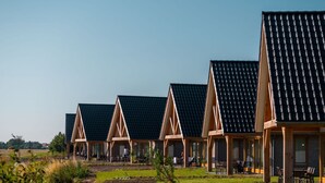 A row of modern, triangular-roofed buildings with outdoor seating areas and a well-maintained lawn. - Luxury Dune Villa on a Holiday Park (Cadzand-Bad)