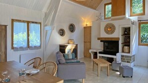 A cozy living room with a fireplace, wooden furniture, and a dining area with chairs and a table set for a meal. - Cozy wooden chalet in the forest, perfect for couples (Chaumont)