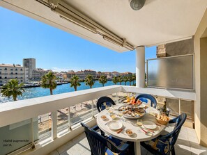 A balcony with a table set for dining, overlooking a marina and cityscape.