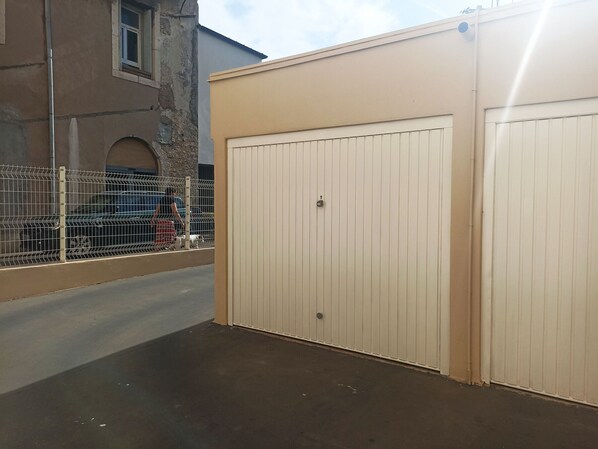 A gated parking area with a concrete floor, a metal fence, and a beige building with a large garage door.