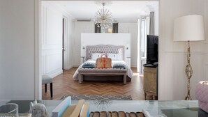 Une chambre à coucher avec une tête de lit capitonnée, un grand lit, une table de chevet, une lampe et un téléviseur.