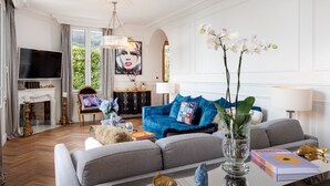 Un salon spacieux avec un grand canapé bleu, un divan gris et une cheminée. On y trouve également une télévision, un lustre et un tableau accroché au mur.