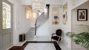 Un vaste hall d’entrée avec un sol en marbre, un lustre, un escalier et un grand miroir.