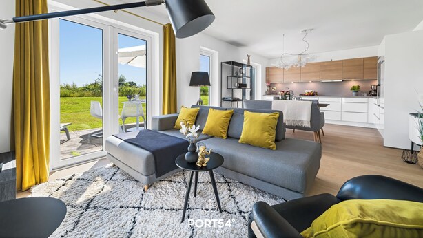 Un salon moderne avec un canapé gris, des coussins jaunes, un lampadaire noir et une table basse noire sur laquelle est posé un vase.