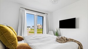 Une chambre moderne avec un grand lit, un téléviseur fixé au mur et une fenêtre avec des rideaux.