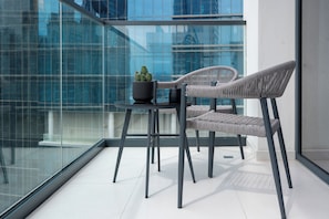 Un balcon moderne avec une paroi en verre, deux fauteuils en osier, une petite table et une plante en pot.