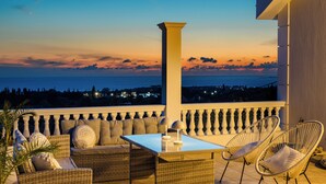 Un balcón con mobiliario de mimbre, una mesa y vistas al mar al atardecer.