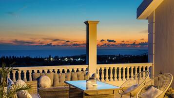 Un balcon agrémenté de meubles en osier, d’une table et offrant une vue sur la mer au crépuscule.