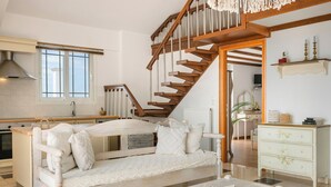 Un amplio salón con una escalera de madera, un sofá blanco y una mesa de comedor.