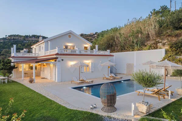 A modern house with a swimming pool, outdoor seating, and a well-maintained garden. - Pantheon Villa (kefalonia)