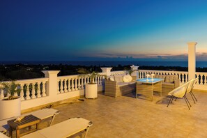 A terrace with a view of the city skyline at dusk, featuring outdoor furniture and a white balustrade. - Pantheon Villa (kefalonia)