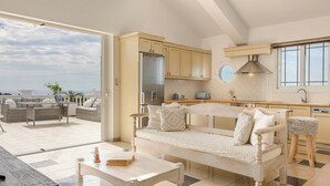 Una cocina moderna con horno integrado, un área de comedor con sofá y mesa blancos, y vistas al exterior.
