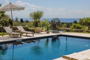 A pool area with lounge chairs, a hanging chair, and a view of the sea. - Pantheon Villa (kefalonia)