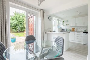 Enjoy meals at the glass dining table with two comfortable chairs, surrounded by a beautiful garden view.