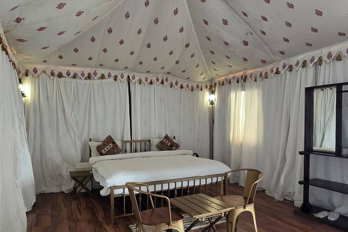 A tented room with a bed, wooden floor, and a table with chairs.
