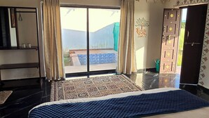Une chambre d’hôtel avec un grand lit, une vue sur une piscine et une porte ornée d’un motif décoratif.