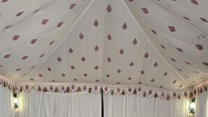 Une pièce aménagée avec une tente, un lit, deux chaises, une table et des rideaux à motifs.