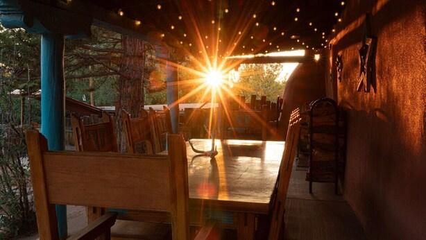 A wooden table with chairs under a string-lit ceiling, with a bright light source in the background. - The Star House in Taos (Taos)