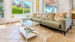 A modern living room with a sofa, a glass coffee table, and a view of greenery outside. - Petramar by Interhome (Lloret de Mar)