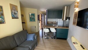 A compact living space with a sofa, a dining area with two chairs, a kitchen with modern appliances, and a surfboard mounted on the wall.