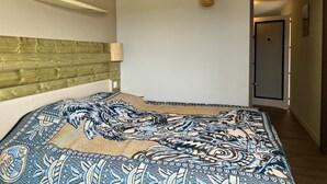 A bedroom with a wooden headboard, a patterned bedspread, a hanging basket, and a door to the right.