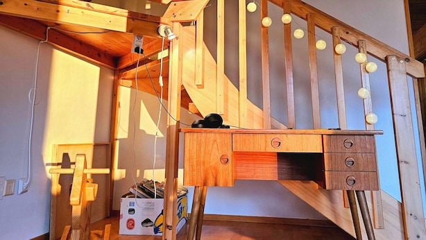 Un escalier en bois avec un bureau et des tiroirs, des poutres en bois et des ampoules suspendues.