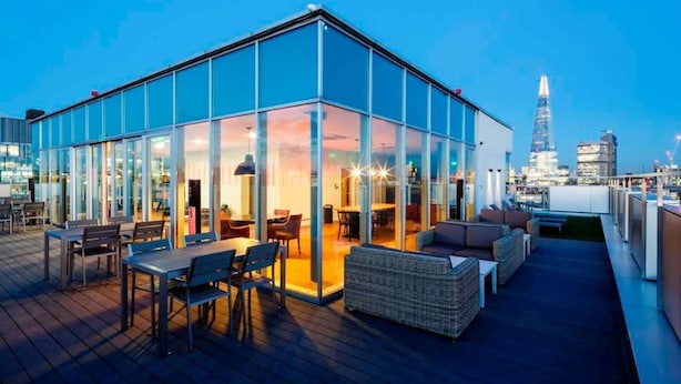 A modern glass building with a rooftop terrace featuring outdoor seating and a view of the city skyline. - For Students Only Chapter South Bank in London (London)