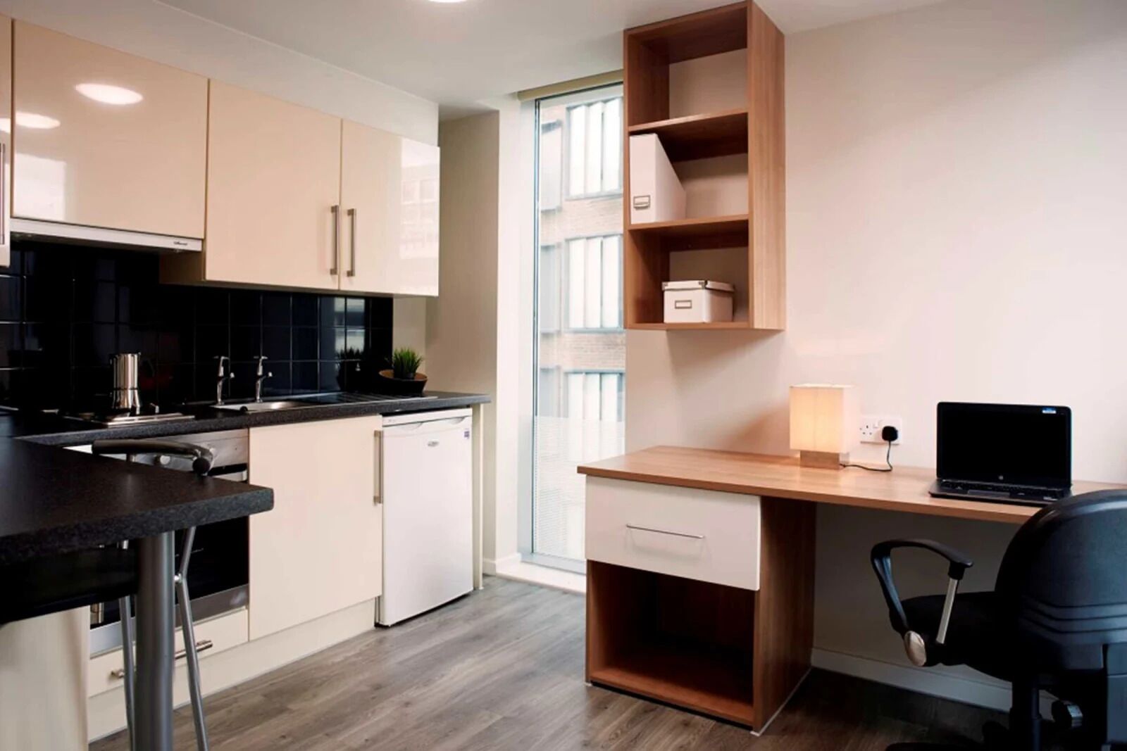 A modern kitchen with a built-in dishwasher, a wooden desk with a laptop, and a chair.