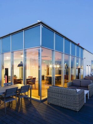 A modern building with large glass windows, outdoor seating area with wicker furniture, and a visible interior with tables and chairs. - For Students Only Chapter South Bank in London (London)