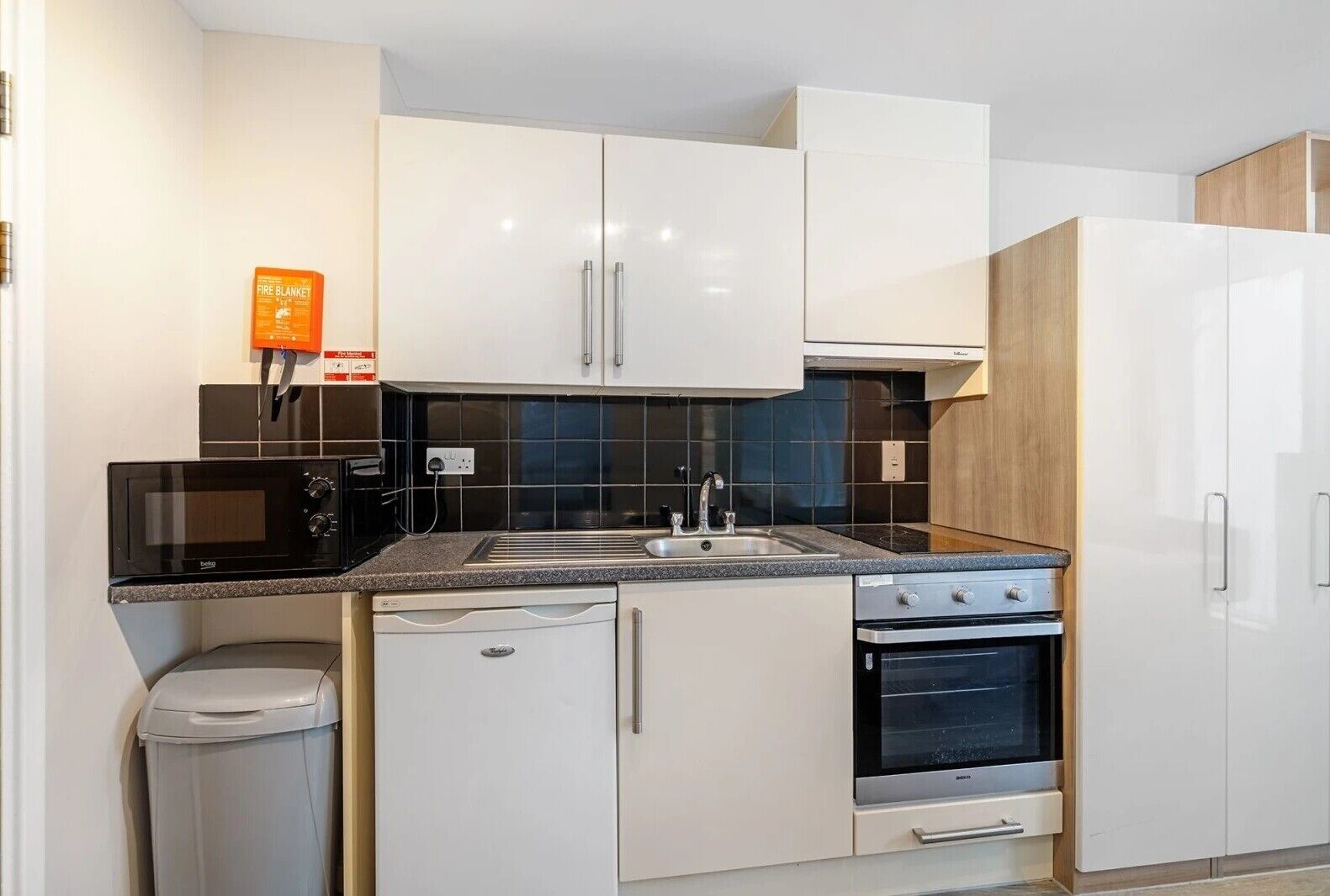 A modern kitchen with white cabinets, a black microwave, a sink, and a stove.