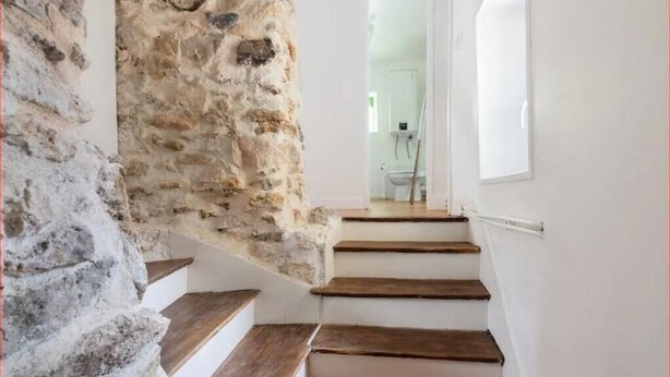 A staircase with stone walls and wooden steps leading to a room with a white door and a window. - “Keep the magic going after Disney” (Saint-Germain-sur-Morin)
