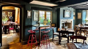 A traditional pub with exposed wooden beams, a bar area with stools, and a fireplace. - The Crown at Shipton (Chipping Norton)