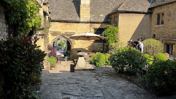 A stone-paved courtyard with traditional stone buildings, a stone bench, and a small archway. - The Crown at Shipton (Chipping Norton)