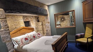 A bedroom with a stone wall, a wooden bed, a mirror, and a chair. - The Crown at Shipton (Chipping Norton)
