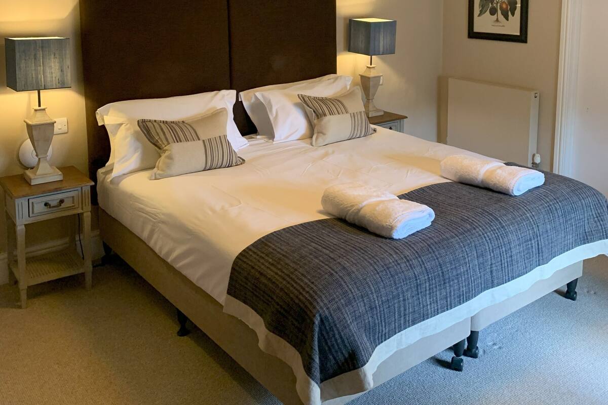 A neatly made bed with white linens and gray accents, flanked by nightstands with lamps and a framed picture on the wall.
