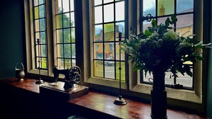 A room with large windows, a vintage sewing machine, a small table, and a potted plant. - The Crown at Shipton (Chipping Norton)