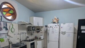 Eine kompakte Küche mit weißen Geräten, einem kleinen Backofen, einer Mikrowelle und einem Kühlschrank. Ein Fenster mit kreisförmigem Muster und eine Deckenleuchte sind vorhanden.