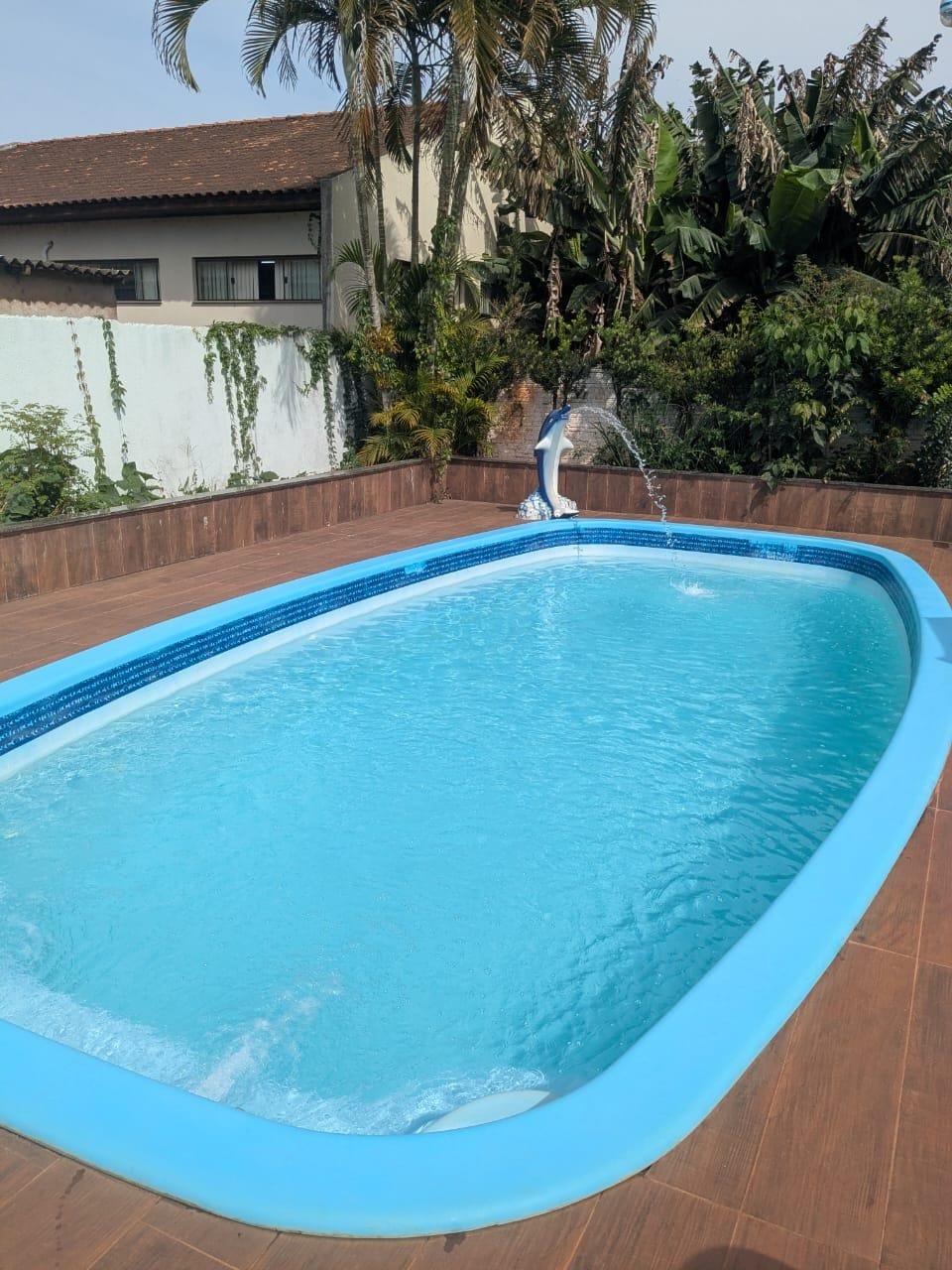 Une piscine rectangulaire à bordure bleue, entourée d’une terrasse en bois et d’un mur blanc agrémenté de verdure.
