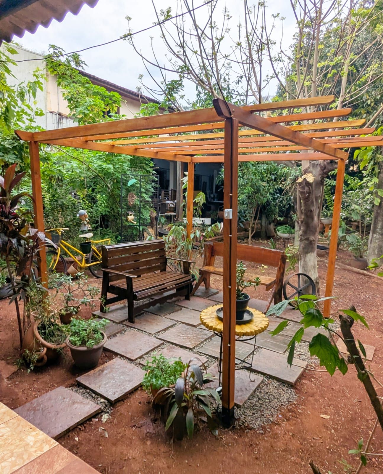 Une terrasse de jardin agrémentée d’une pergola en bois, d’un banc en bois et de plantes en pot.