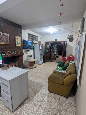 A living room with a sofa, a TV, a fireplace, and a tiled floor. - Melizas Garden (Foz do Iguaçu)