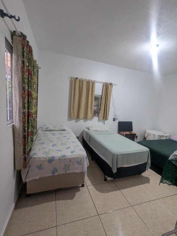 Une chambre avec deux lits simples, une fenêtre avec des rideaux, une table de chevet et un luminaire fixé au mur.