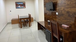 Zona de menjador amb taula i cadires de fusta, un quadre a la paret, televisió penjada a un panell de fusta i nevera petita sota la taula.