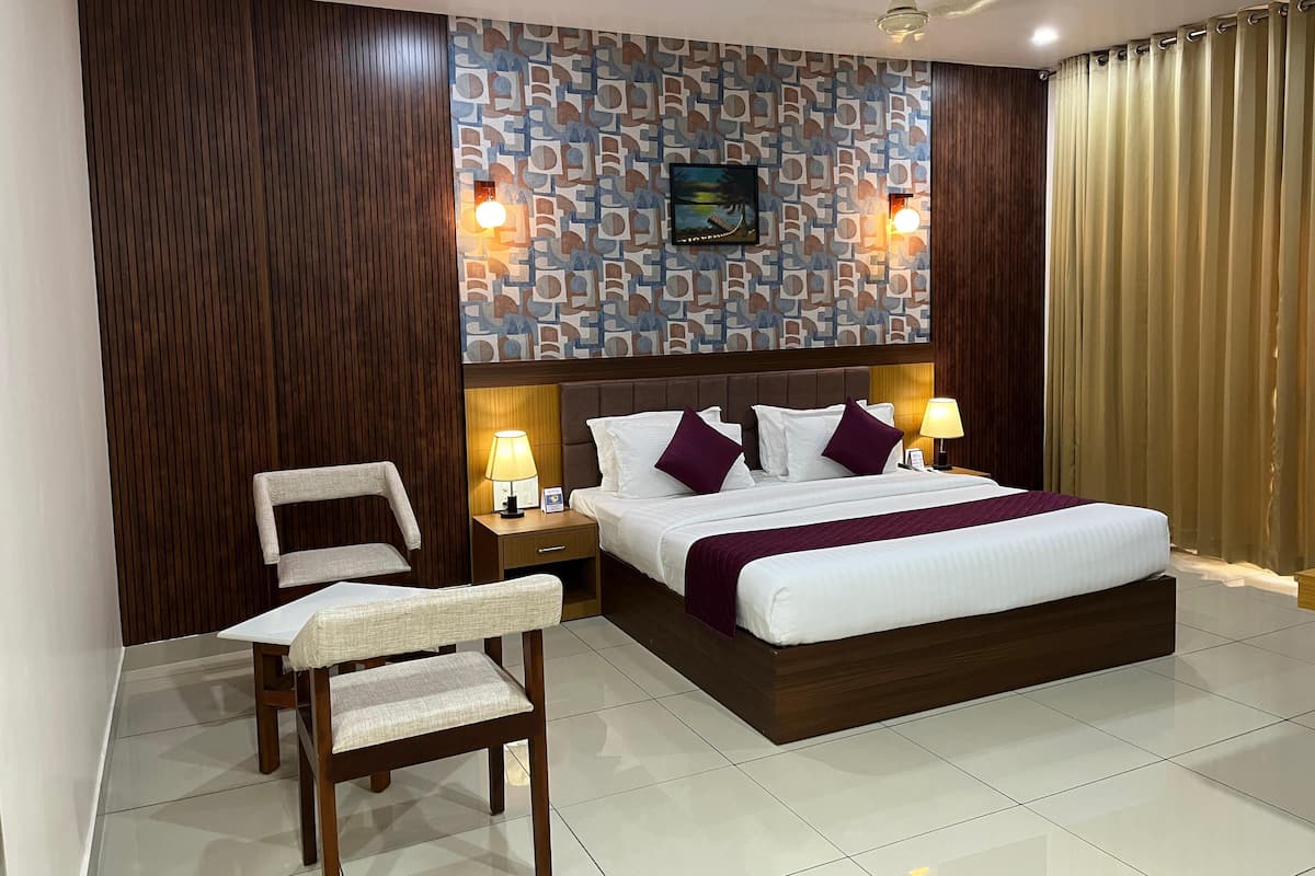 A hotel room with a large bed, two bedside tables with lamps, a chair, a patterned wall, and a ceiling fan.