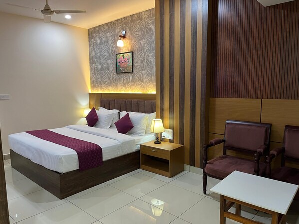 A hotel room with a large bed, two bedside tables, a chair, and a small table. - Hotel Floral Palace (Kottayam)