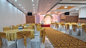 Una sala de banquetes amb files de taules i caires, una catifa amb dibuixos i un escenari decorat amb flors.