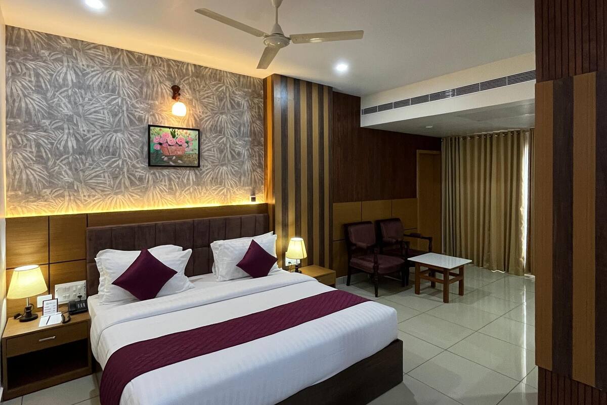 A hotel room with a large bed, a ceiling fan, a wall-mounted TV, and a small table with chairs.
